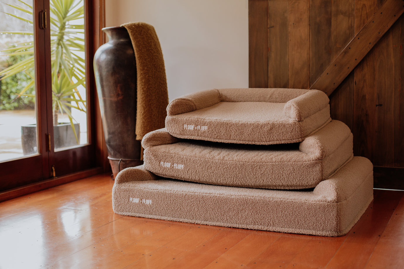 Stack of beige Floof n Fluff Dog beds on a wooden floor in a warm living room